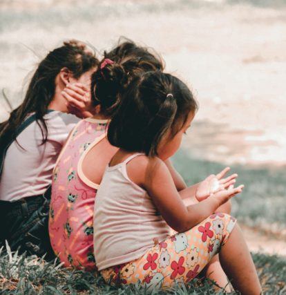 three children sitting on a grassy hill