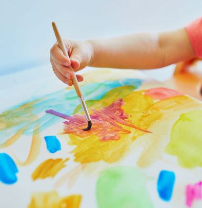 a child holding a paint brush and painting on a colourful piece of paper