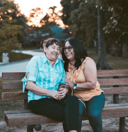 two women holding each other and laughing on a park bench