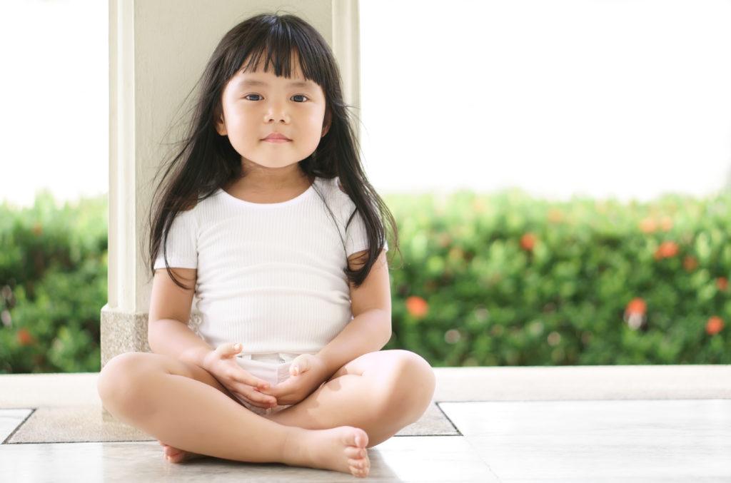 a child with black hair and bangs sitting cross legged on a white floor